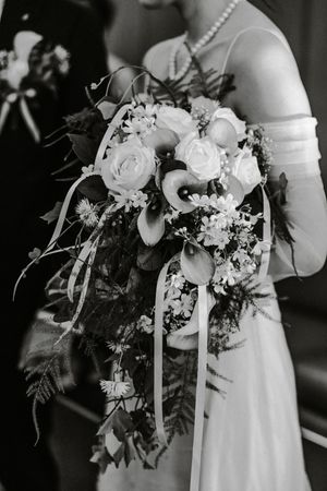 Beautiful wedding bouquet featuring white calla lilies, roses and delicate greenery in a cascading arrangement.