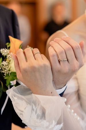 Close-up of hands wearing formal white gloves and wedding rings during ceremony.