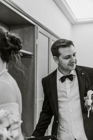 Close-up black and white photo of a groom at a formal wedding in a tuxedo and white vest.