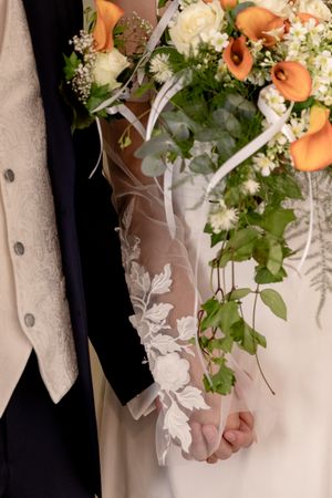 Elegant wedding bouquet with orange calla lilies and cascading greenery against white fabric.