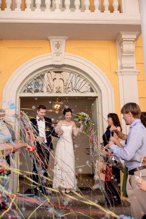 Festive wedding exit with streamers and confetti outside a yellow building with classical architecture.