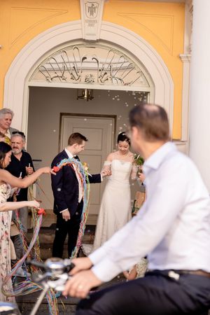Guests celebrating with colorful streamers outside a sunny yellow building with white columns.