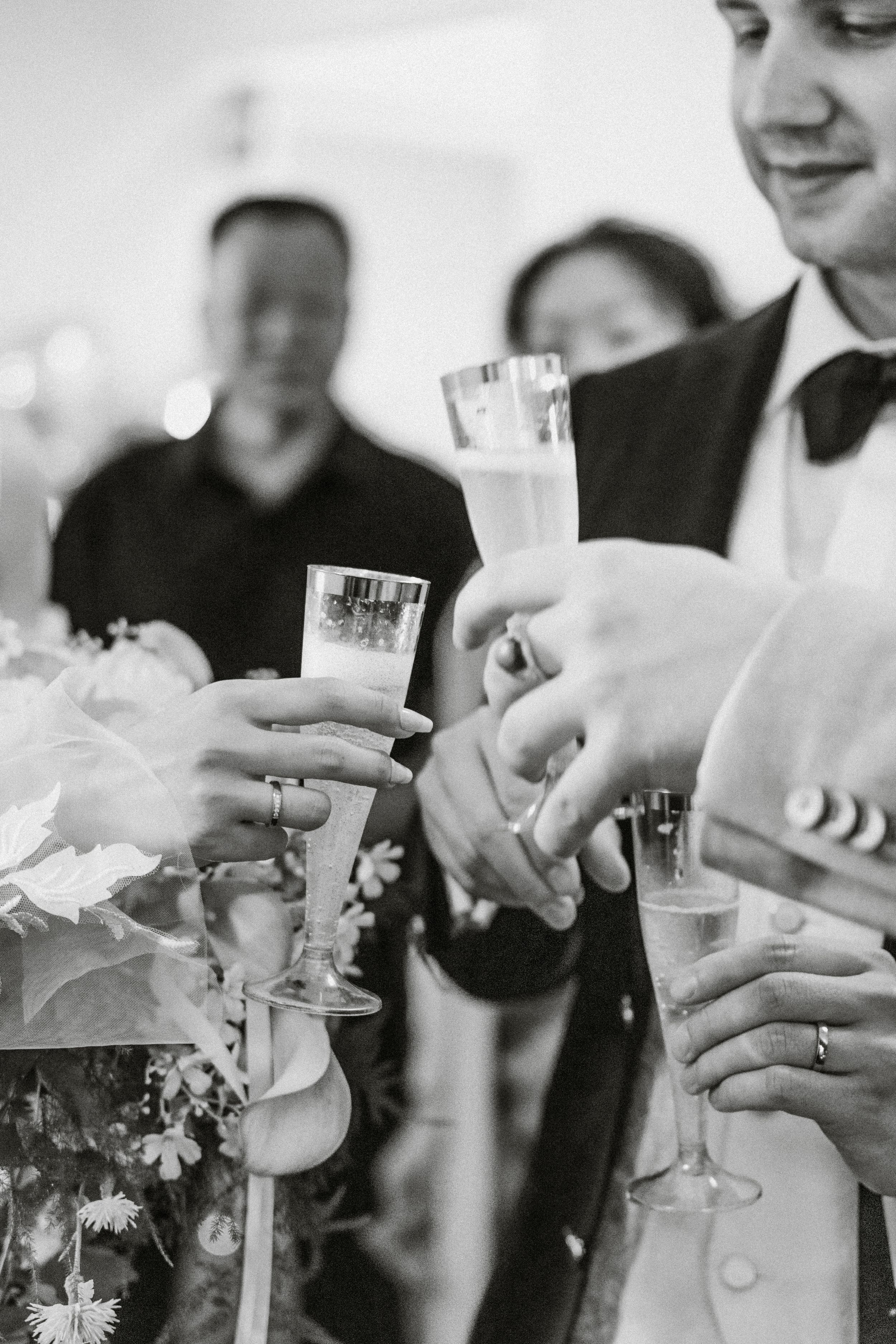 Close-up of wedding guests holding champagne glasses in formal attire.