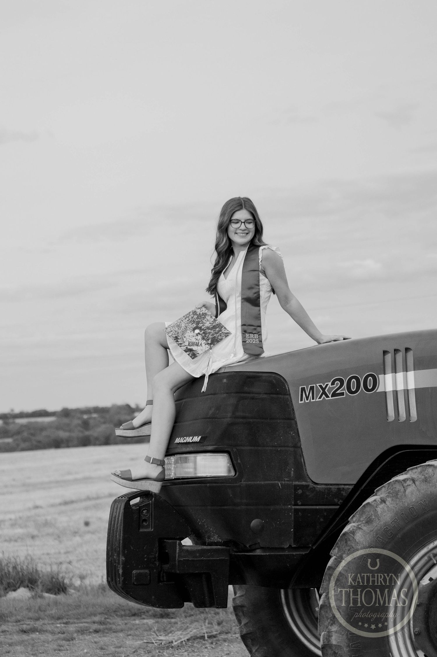 A black and white photograph shows someone seated on a Case MX200 tractor in a rural field setting.