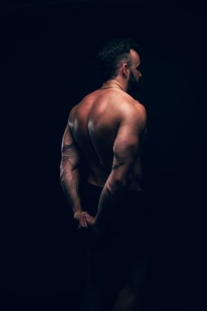 Muscular shirtless man showing back muscles in dramatic dark studio lighting.