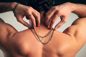 Man clasping gold chain necklace behind neck, showcasing back muscles.