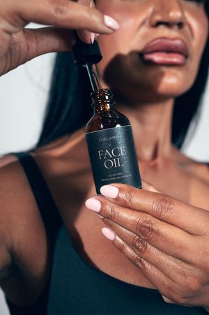 Woman holding Carl James Face Oil dropper bottle close-up beauty shot.