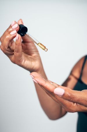 Close-up of woman's hands holding a dropper with golden face serum oil.