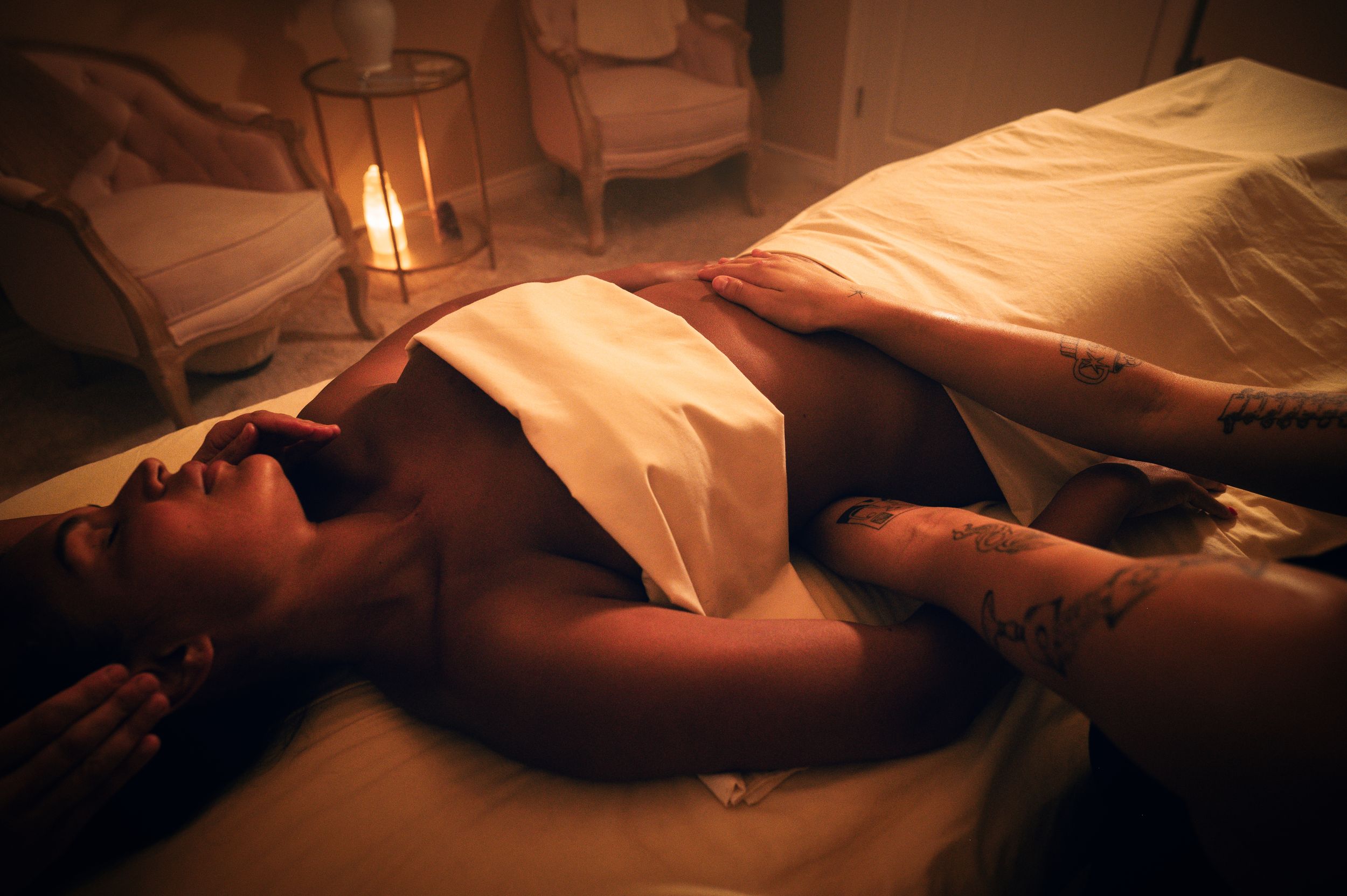 A relaxed client lying on a massage table in a softly candlelit spa room during a therapeutic massage session.