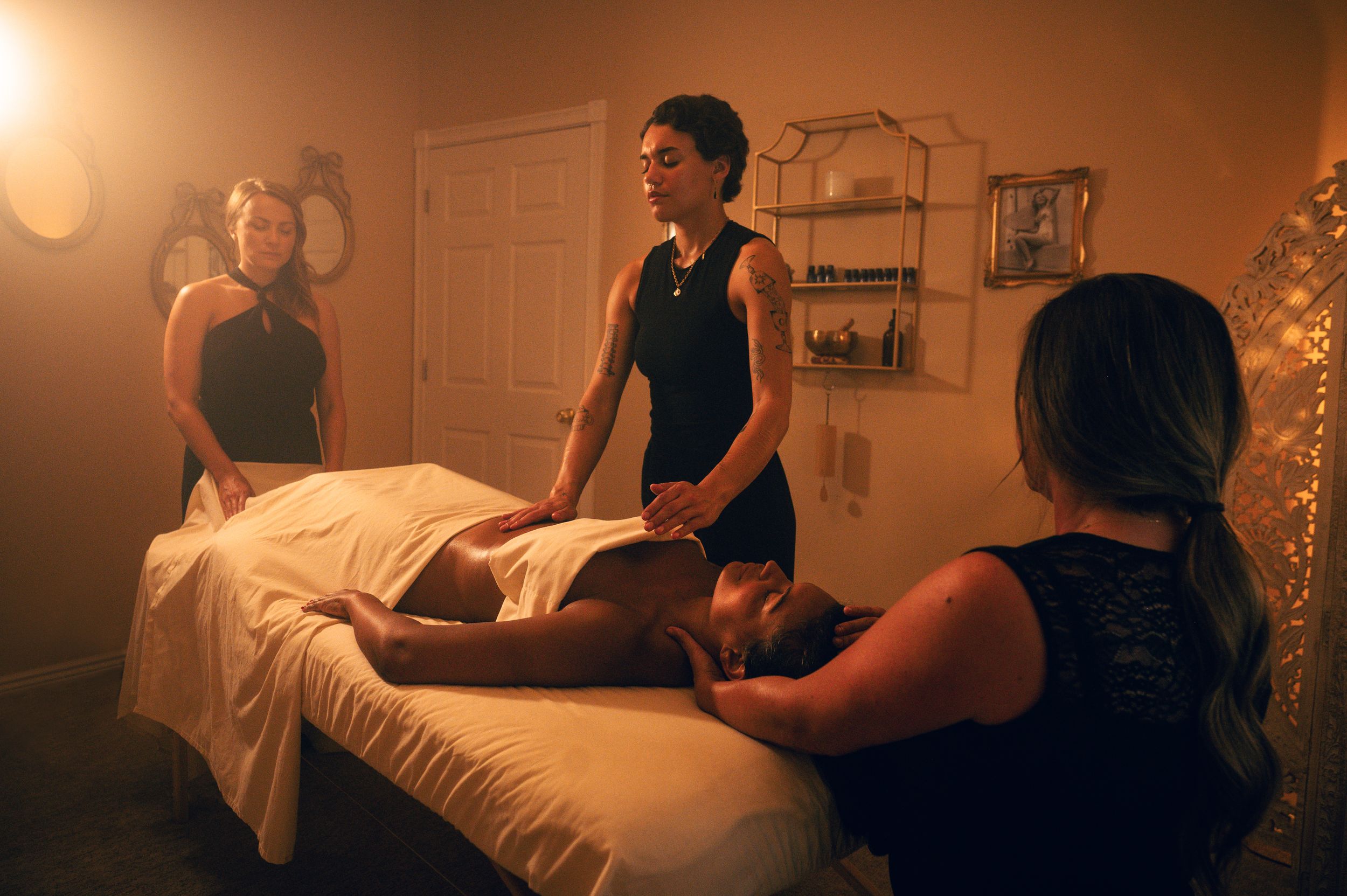 Three massage therapists providing a full-body massage treatment to a client in a warmly lit spa setting.