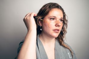 Young woman with freckles applying gold face gems to her hair and face.