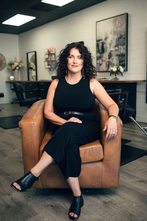 Woman in black outfit sitting confidently in leather chair inside modern hair salon.