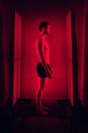 Man standing in red light therapy panel device in darkened room.