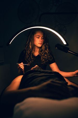 Esthetician performing facial treatment under curved LED light in dark treatment room.