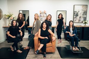 Group of seven salon professionals posing together in modern hair salon interior.