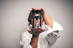 Woman in white shirt holding hourglass in front of face, concept of time.
