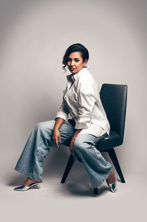 Stylish woman in white shirt and wide-leg jeans posing on modern chair.
