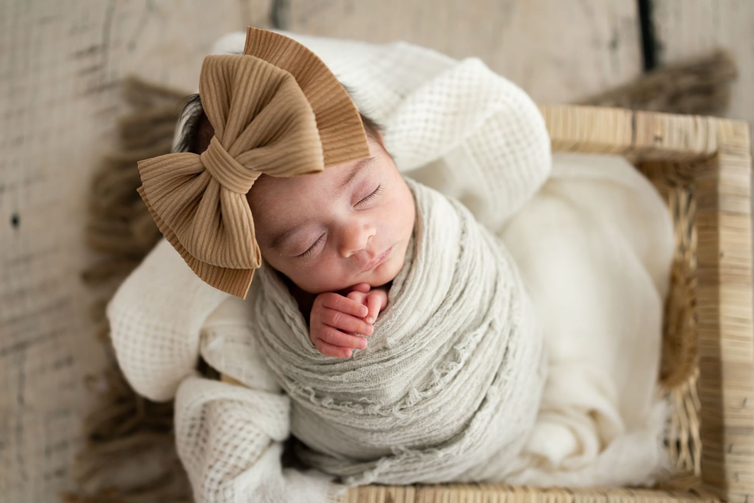 Adorable sleeping newborn baby wearing warm knit clothing and accessories in soft neutral tones.
