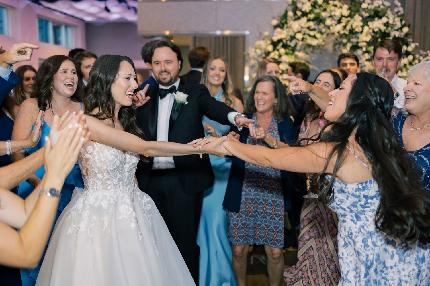 A wedding party wearing black formal attire gathers and laughs together on a columned porch at Current at Pier 59 in New York City.