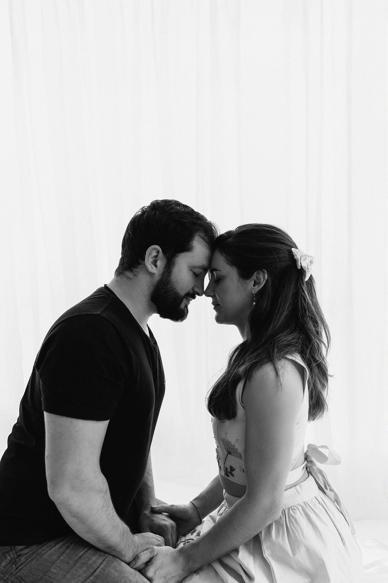 A tender black and white portrait of a couple sharing an intimate forehead touch moment against a light background.