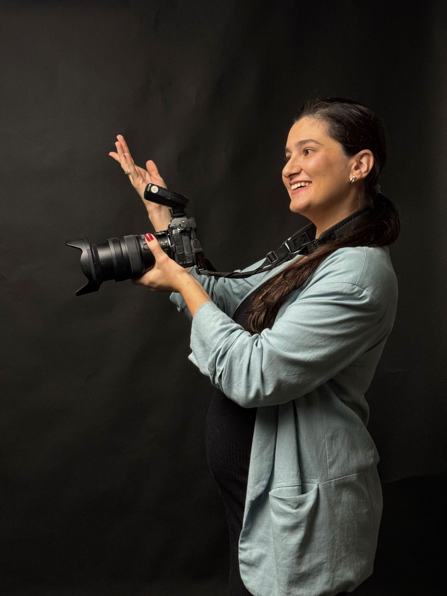 Side profile of photographer in casual light blue attire holding professional camera with telephoto lens against dark backdrop.
