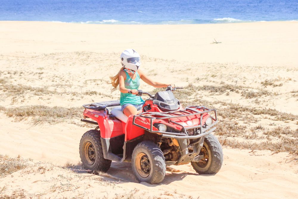 A series of ATV off-road vehicles driving across sandy terrain against a blue sky background.