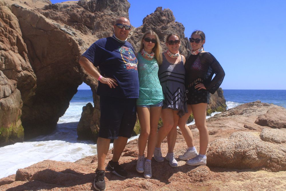 Group standing on red rocky cliffs overlooking scenic Prince Edward Island coastline on a sunny day.