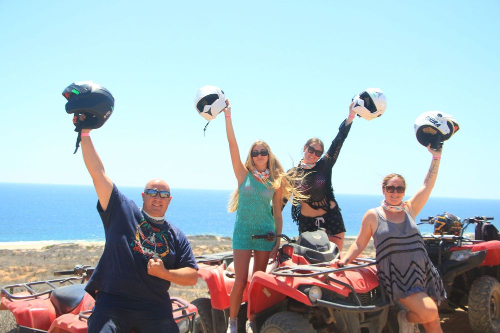 People celebrating and posing excitedly with raised arms against a scenic ocean backdrop during an ATV tour.