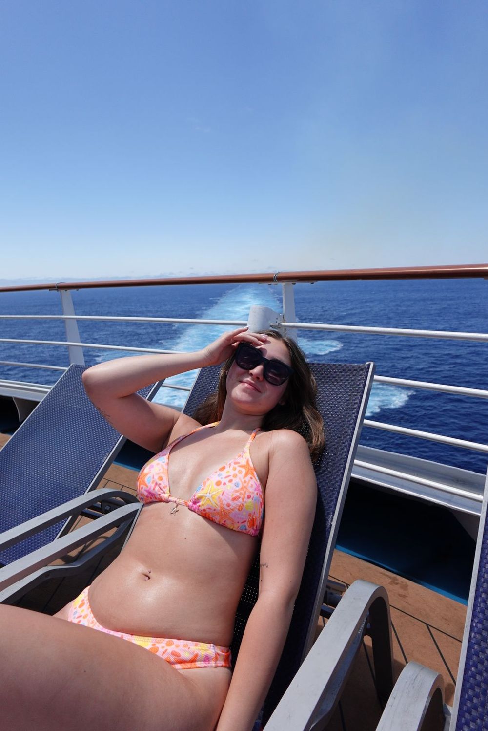 Person sunbathing on a boat deck with blue water and sky visible in the background.