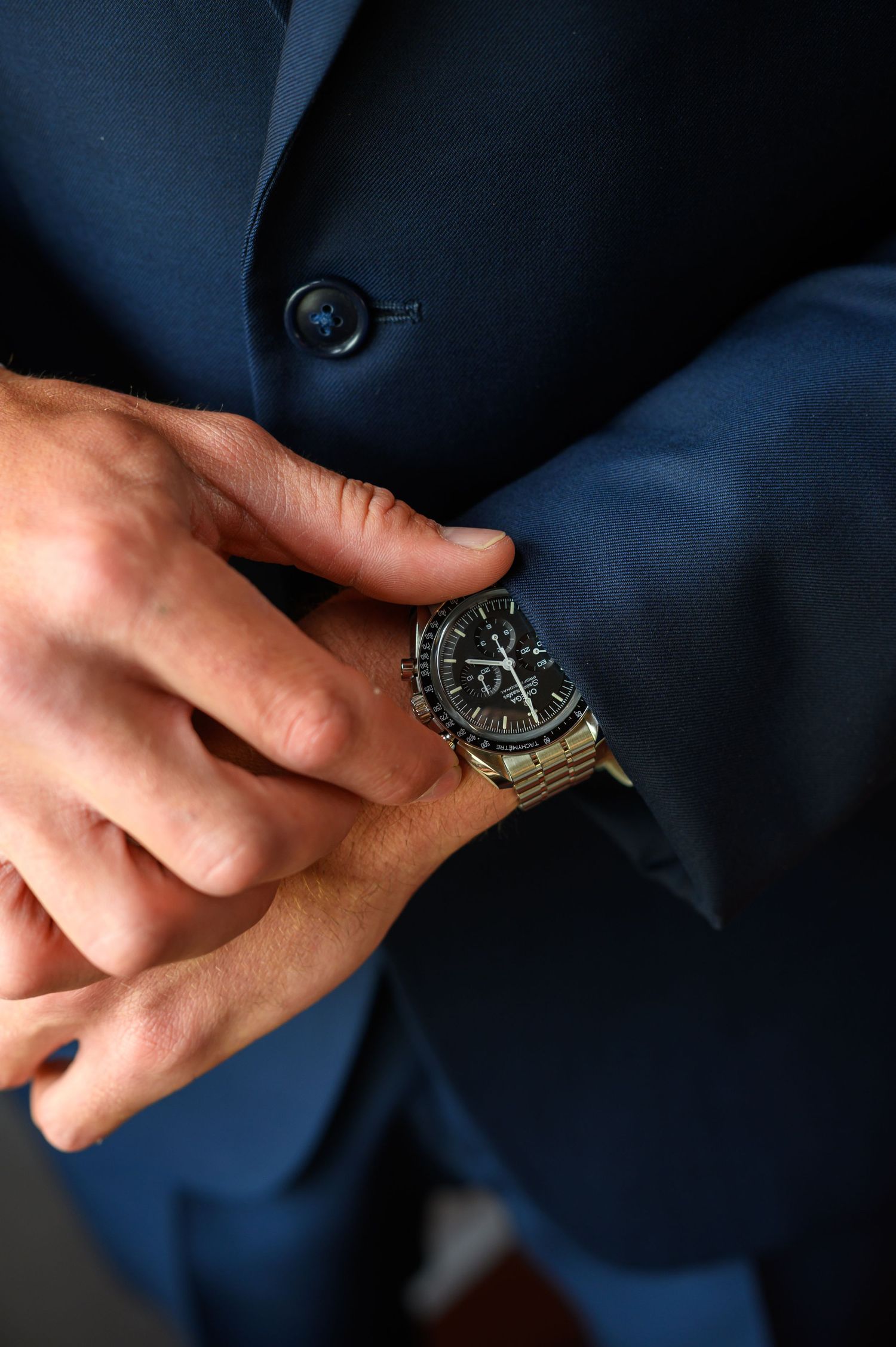 A close-up shot of a wristwatch and hands against a navy blue suit jacket.