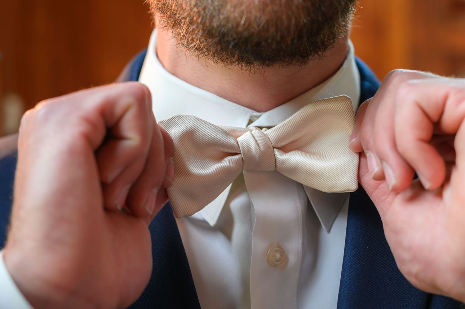 Close-up shot of hands adjusting a white bow tie against a navy suit jacket.