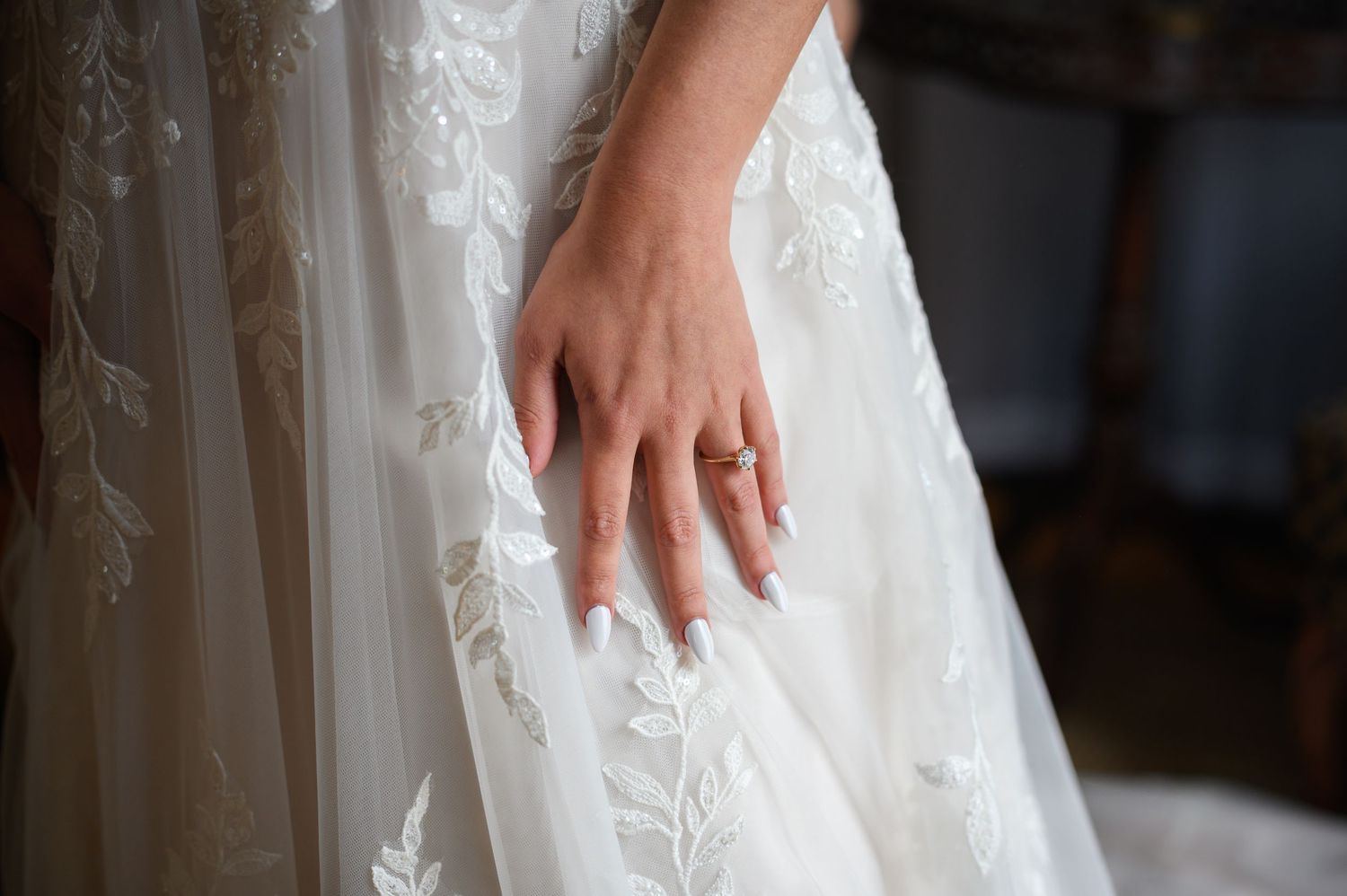 A hand gently touches white lace fabric details on a wedding dress.