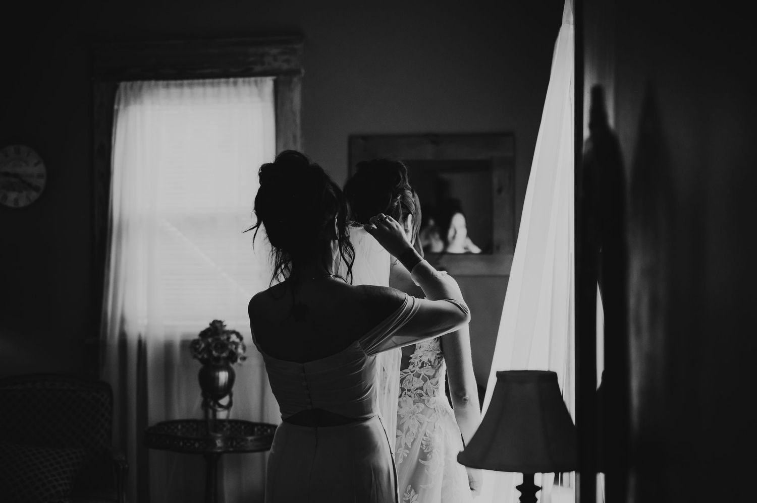 A dark silhouette stands behind curtains in monochromatic lighting creating a moody atmospheric scene.