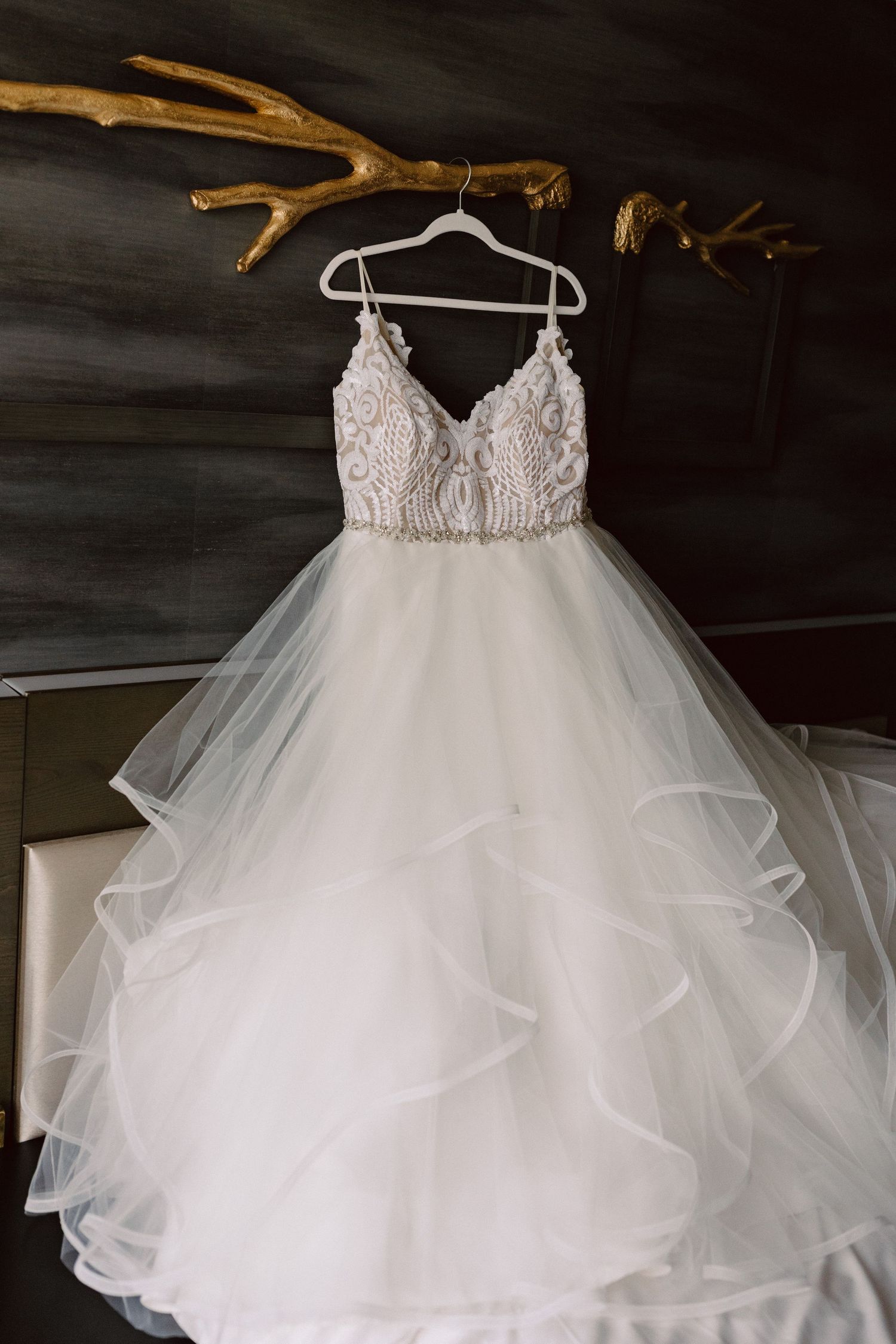 White tulle wedding dress with intricate lace bodice hanging on display.