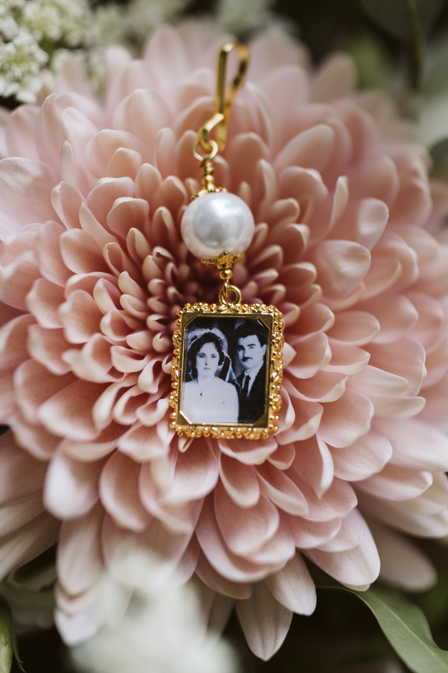 Vintage-style gold locket with pearl accent displayed against soft pink dahlia flowers.