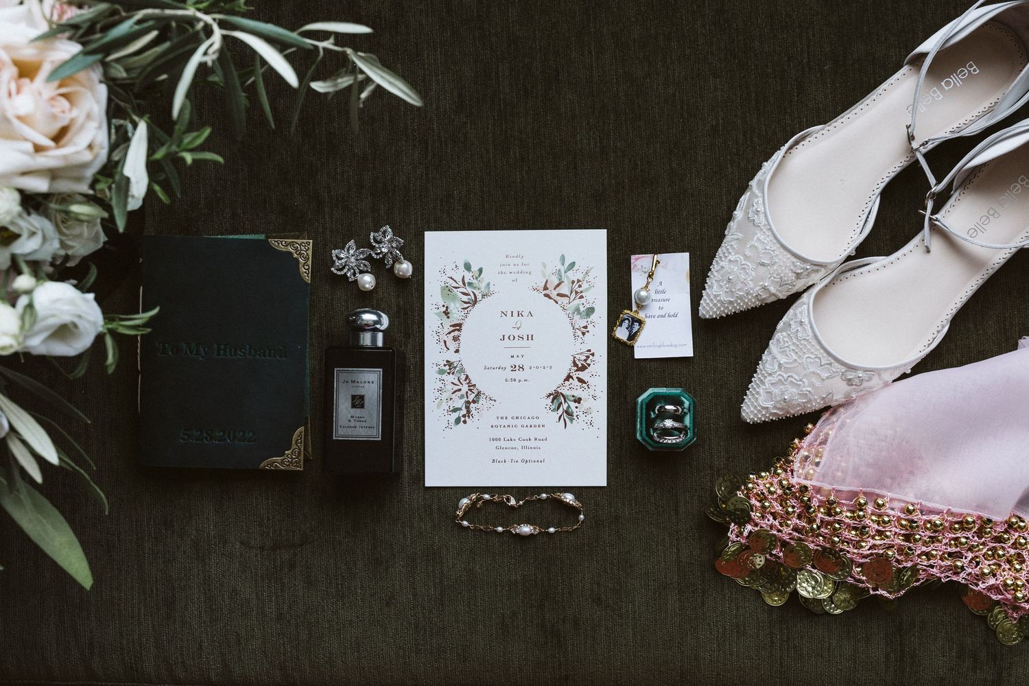 Wedding stationery and detail items arranged on dark background with floral elements.