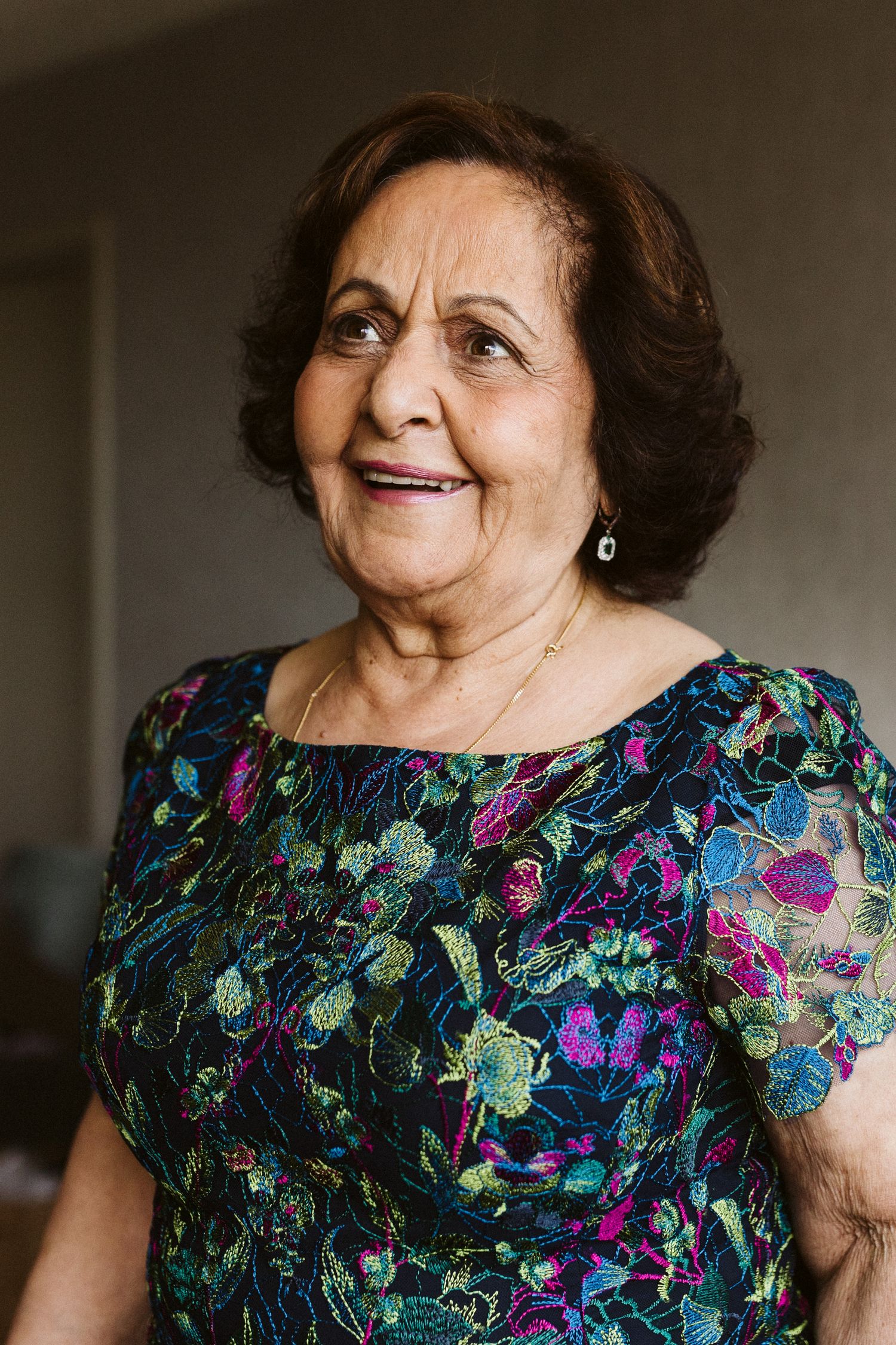 Woman in a floral dress with short sleeves poses against a dark background.