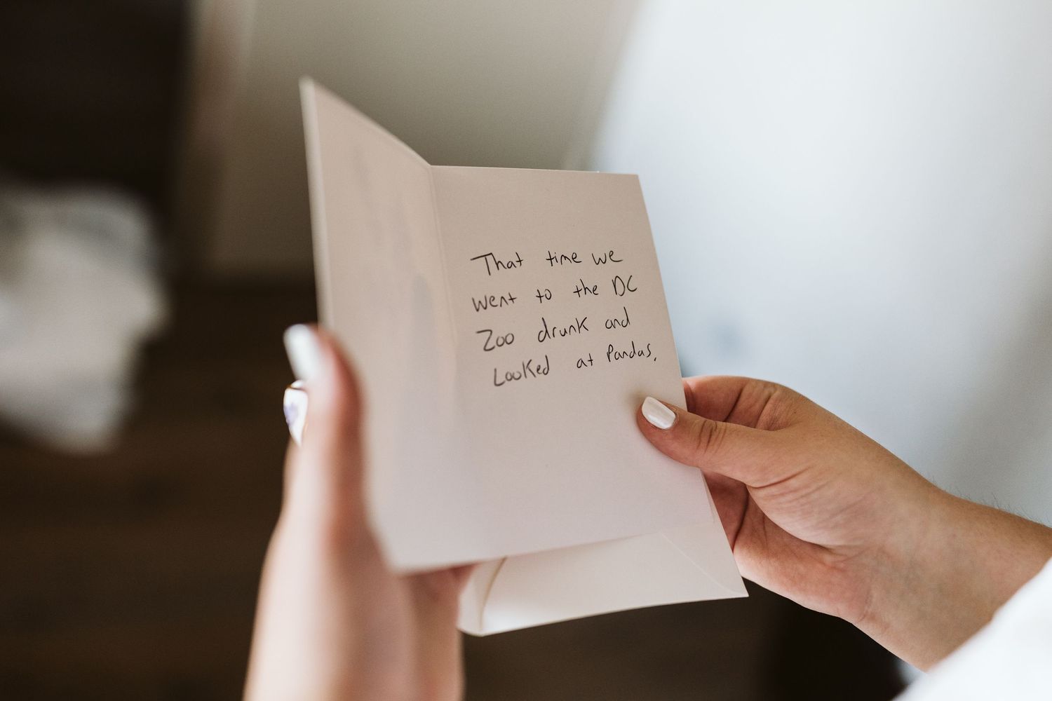 Hands holding a white note card or letter against a light background.