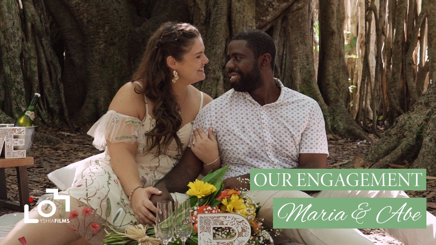 Engagement photo of couple Maria and Abe sitting together under a large tree outdoors.