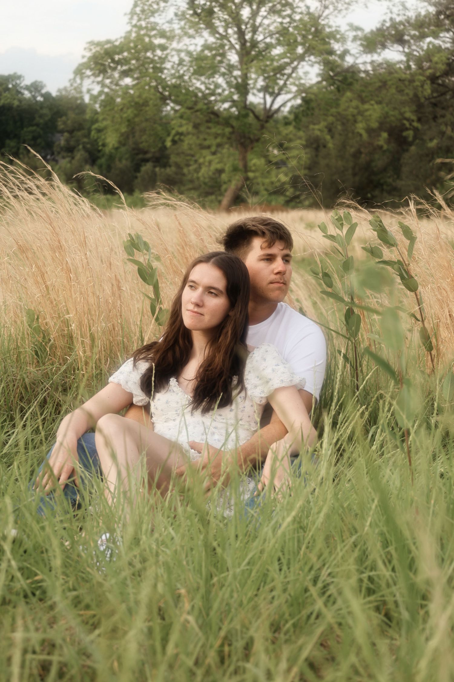 A couple sitting intimately in tall grass during a summer photoshoot.