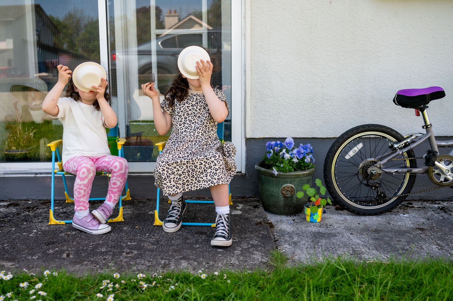 Two people sit outside blowing bubbles next to a bicycle and flower pot on a concrete step.