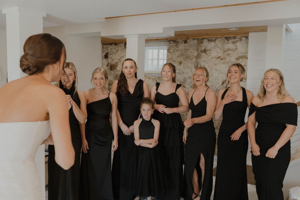Wedding party in black dresses standing together in a bright indoor space.