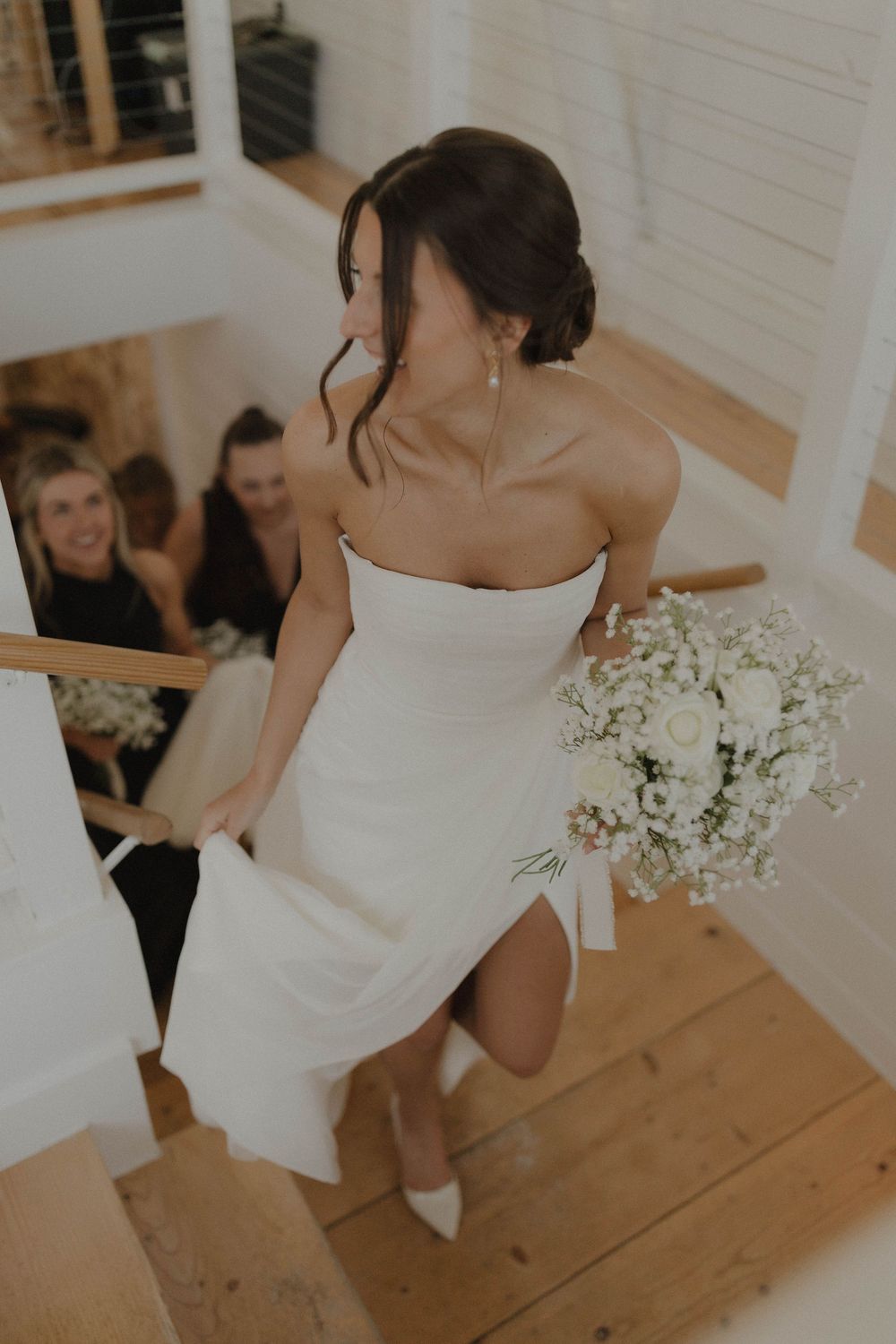 Wedding party poses together on rustic wooden floor with elegant white and floral decor.