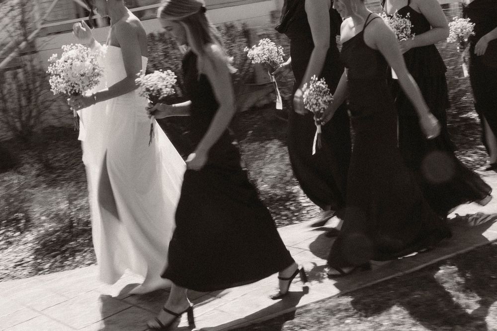 Wedding party relaxes on ground outside white barn venue during photo session.