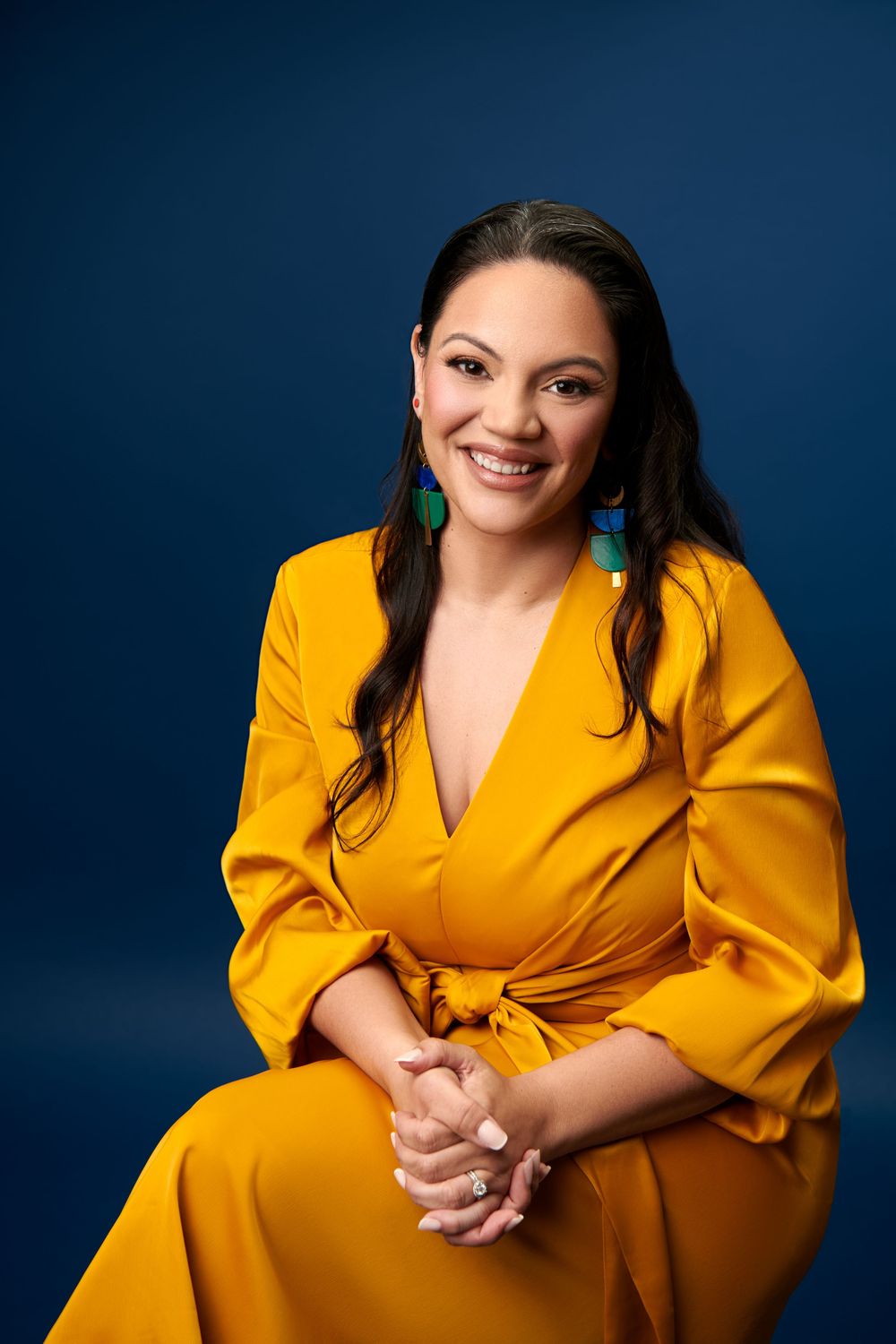Professional studio portrait against blue background wearing bright yellow blazer in dynamic relaxed poses.