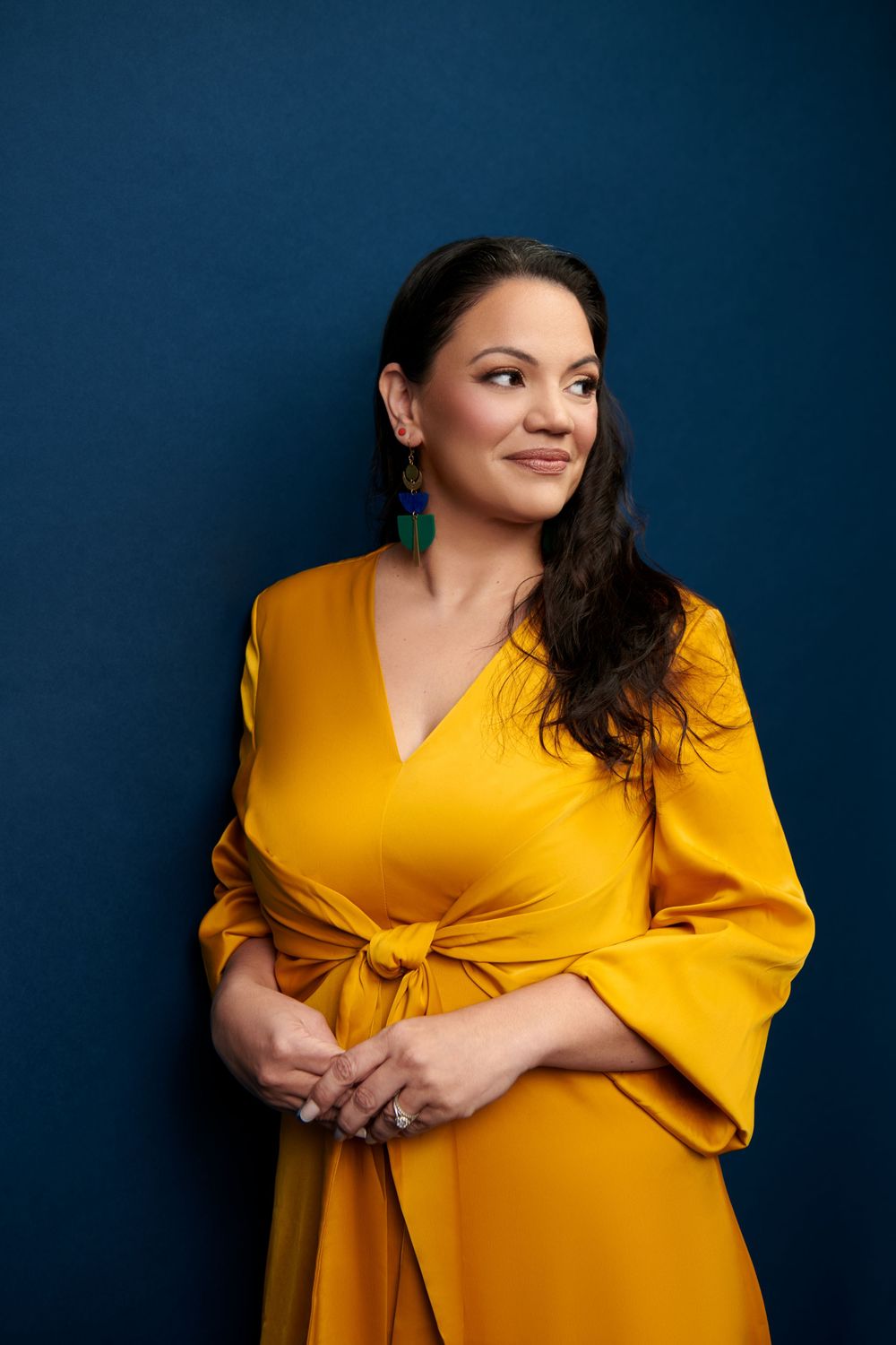 Portrait of a woman in a vibrant yellow dress with bell sleeves against a dark blue background.