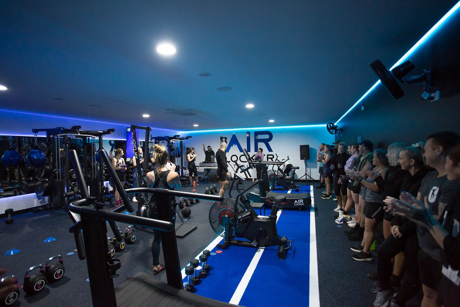 A group of people in black outfits pose together in front of an illuminated blue neon sign at a fitness studio.