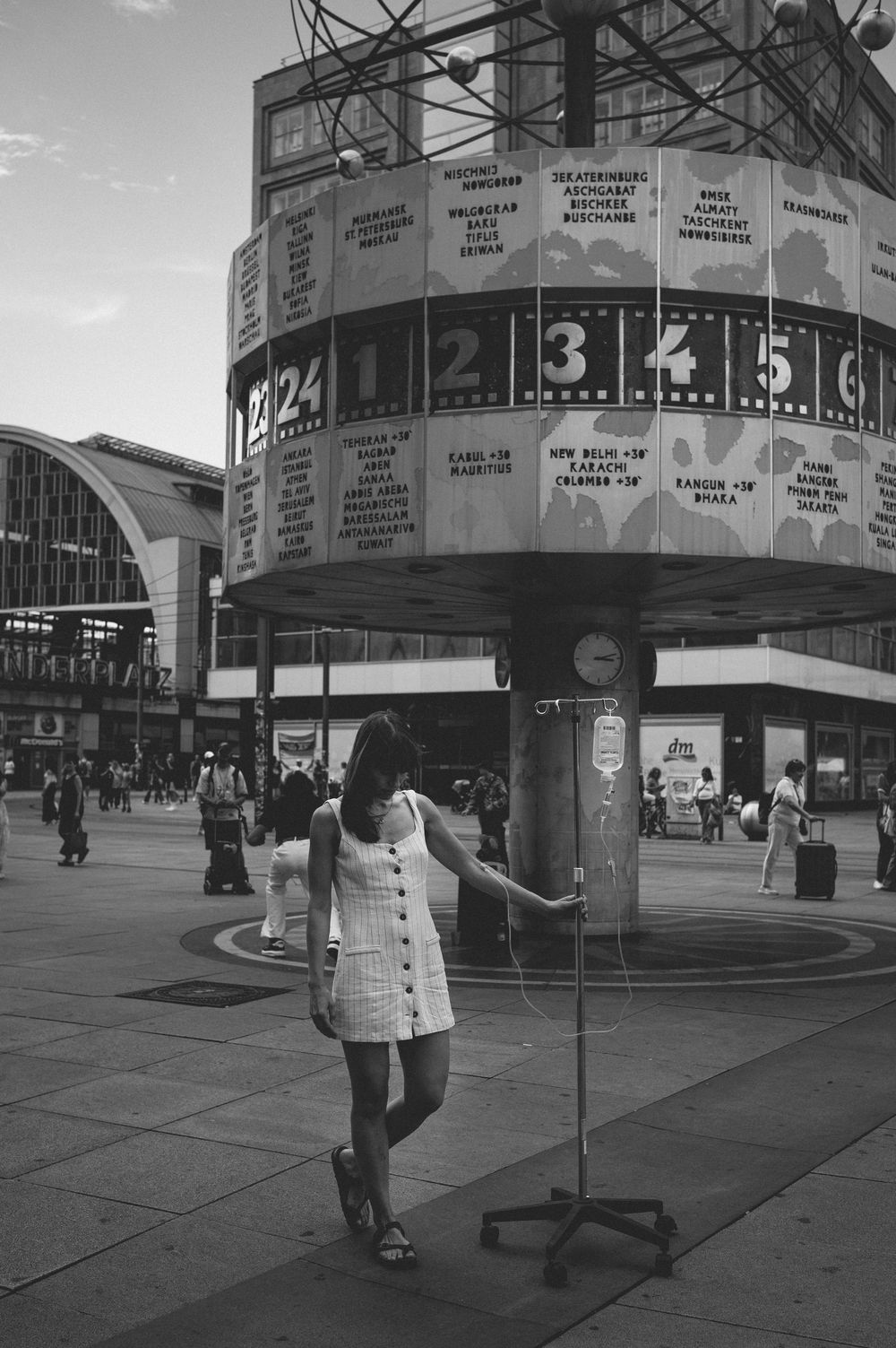 A black and white urban scene with a world clock tower and a figure standing in front of it at Alexanderplatz, Berlin.
