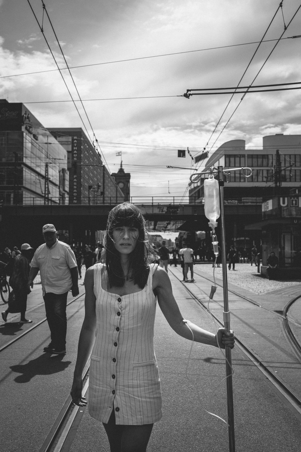 A street scene in Berlin with tram lines, pedestrians, and buildings under cloudy skies captured in black and white.