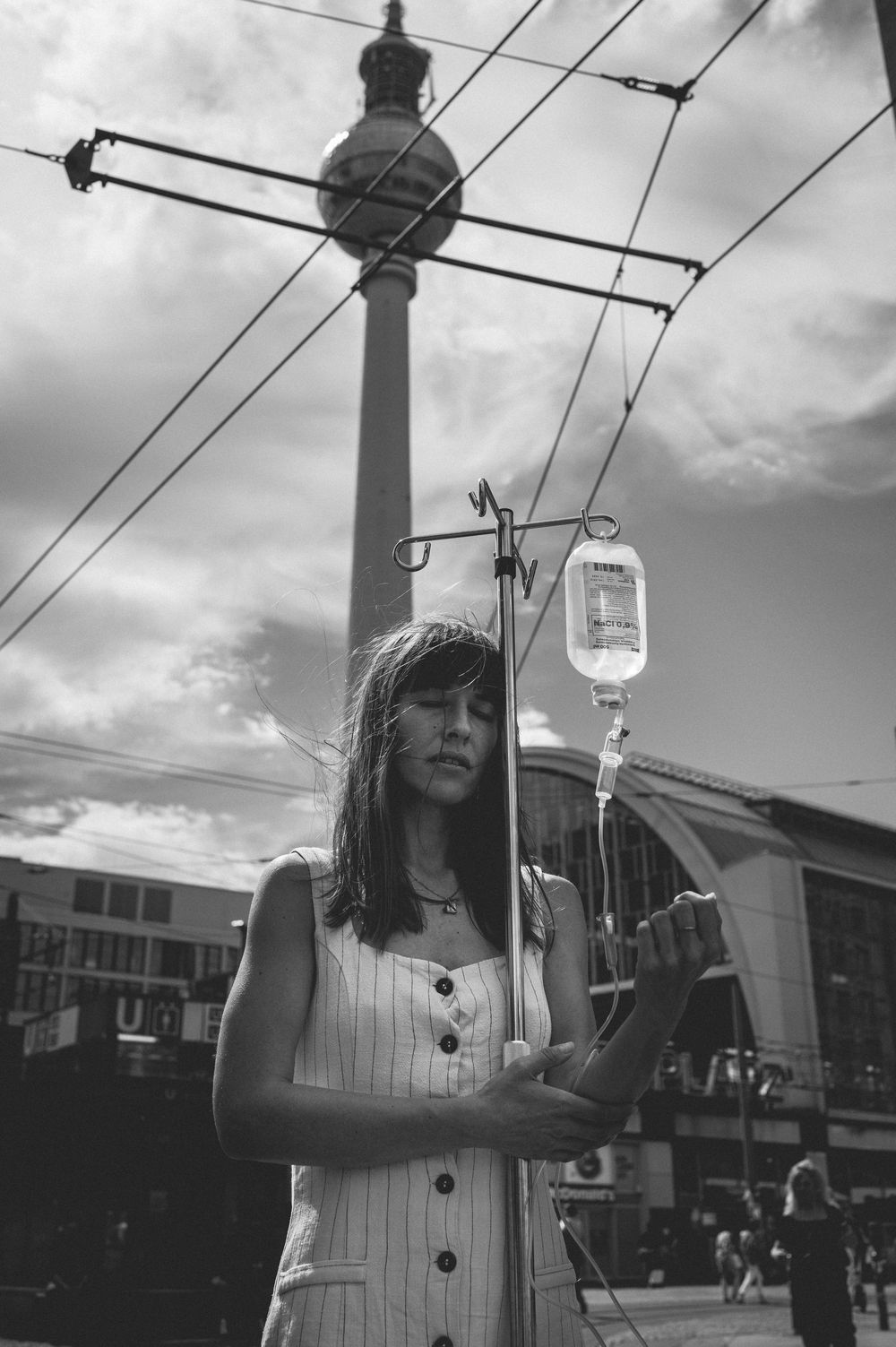 Black and white photo series showing someone holding up an IV bag against power lines and cloudy sky in an urban setting.